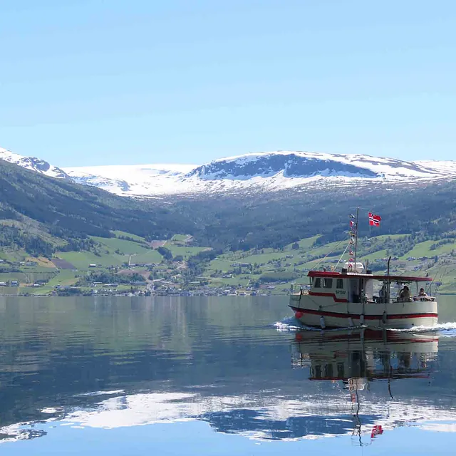En tradisjonell rutebåt som speiler seg på en rolig fjord i Olden.