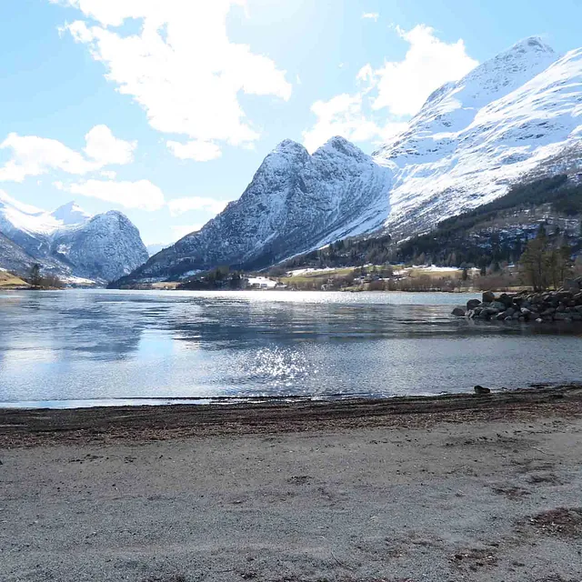 Snødekte fjelltopper som speiler seg vakkert i en rolig innsjø.