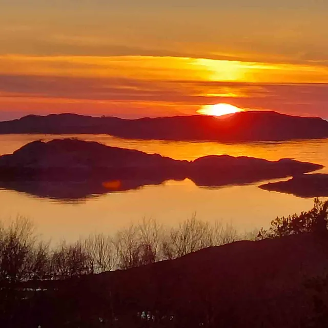 Himmel i dyp rød solnedgang som speiler seg i vannet.