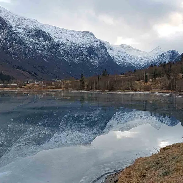 Naturfoto av speilblankt vann omkranset av fjell i Olden.