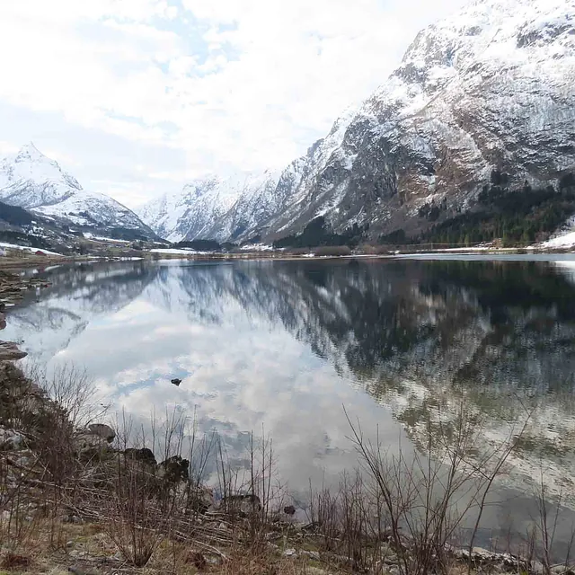 Vinterlandskap der dramatiske, snødekte fjellsider speiles i vannet.