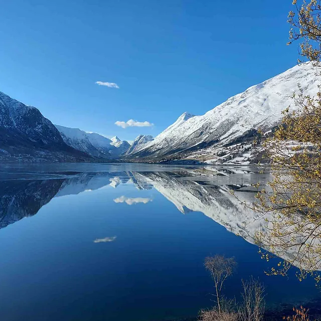 Snødekte fjell som speiler seg i en dypblå innsjø.