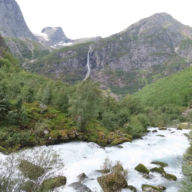 Strykende elv som renner gjennom en grønn dal med fjell og en foss.